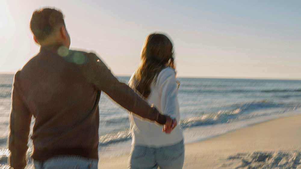 couple holding hands from rear running on sunny beach